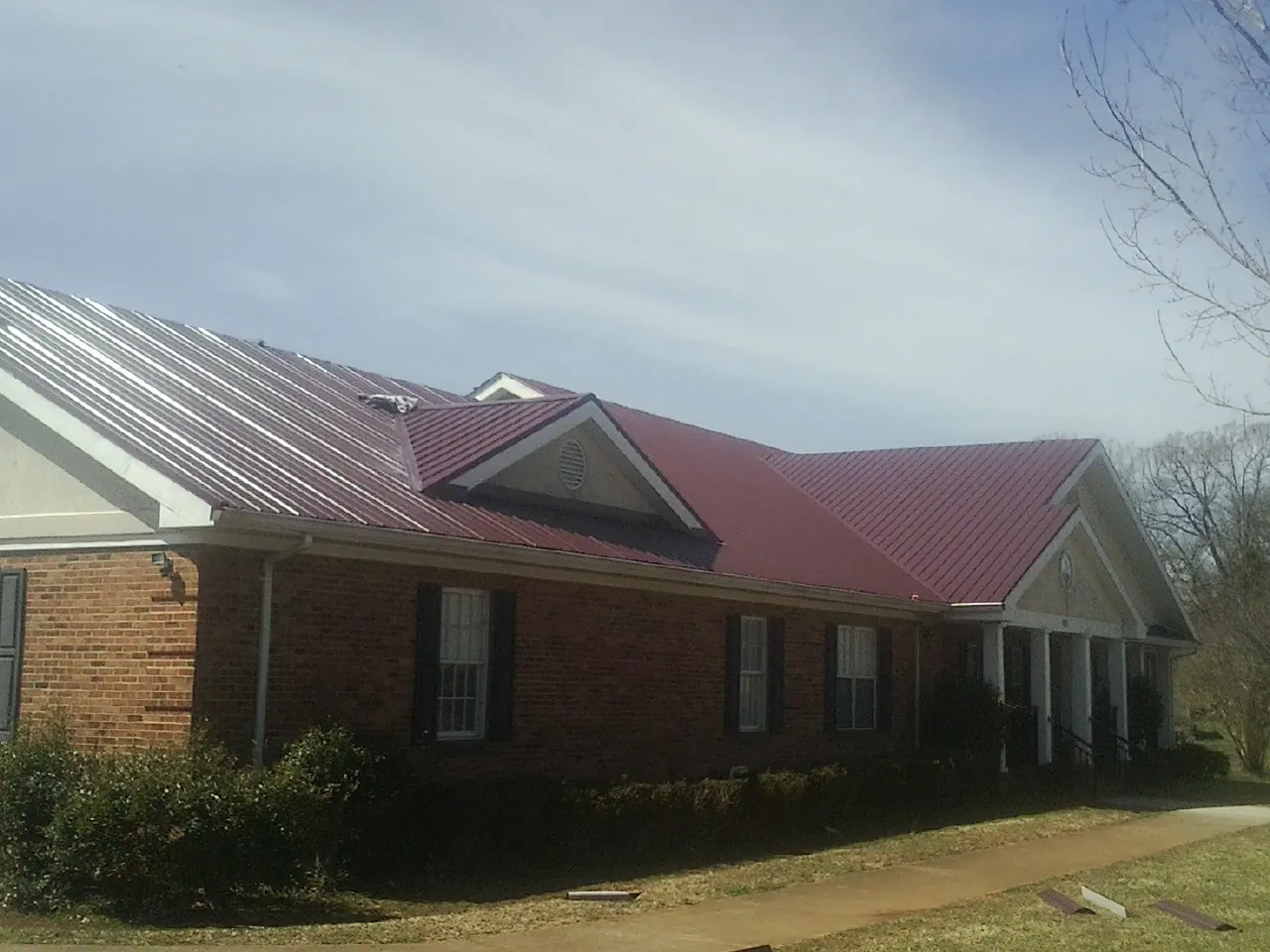Red metal roof with gabled entries on a long brick building, from a Hail Damage Roof Repair job in Fort Washington