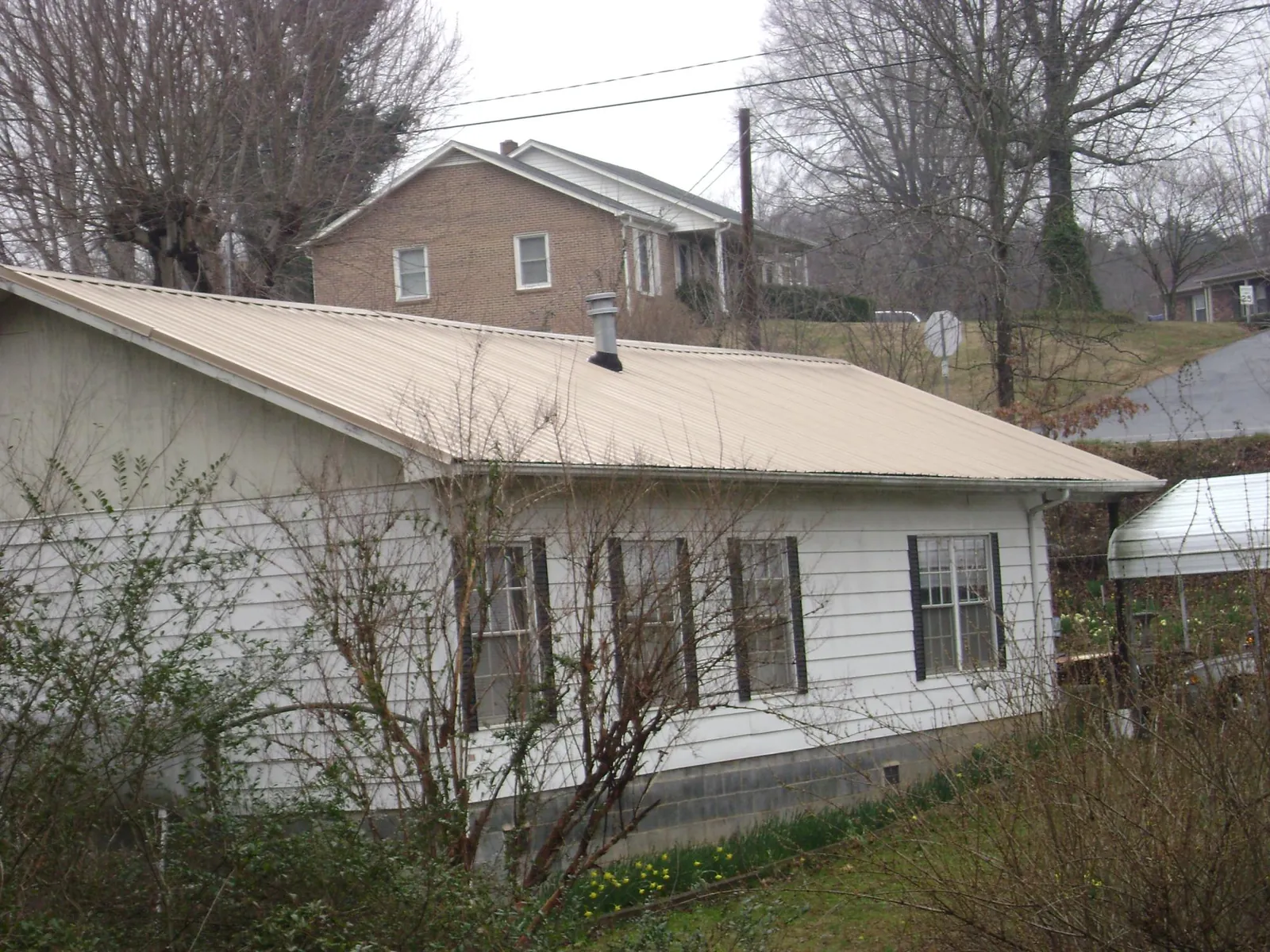 Tan metal roof on a white sided house set into a hillside — Commercial Roofing by Roofing Brothers in Fort Washington